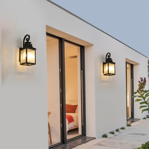 Modern house exterior with open sliding door revealing a bedroom, illuminated by outdoor wall lights.